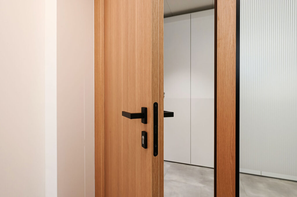 EPICA parete divisoria SLIM pareti vetrate a vetro singolo extra clear con profilo in alluminio jet black ral 9005 e porte a battente con anta cieca in legno colore oak dettaglio porta